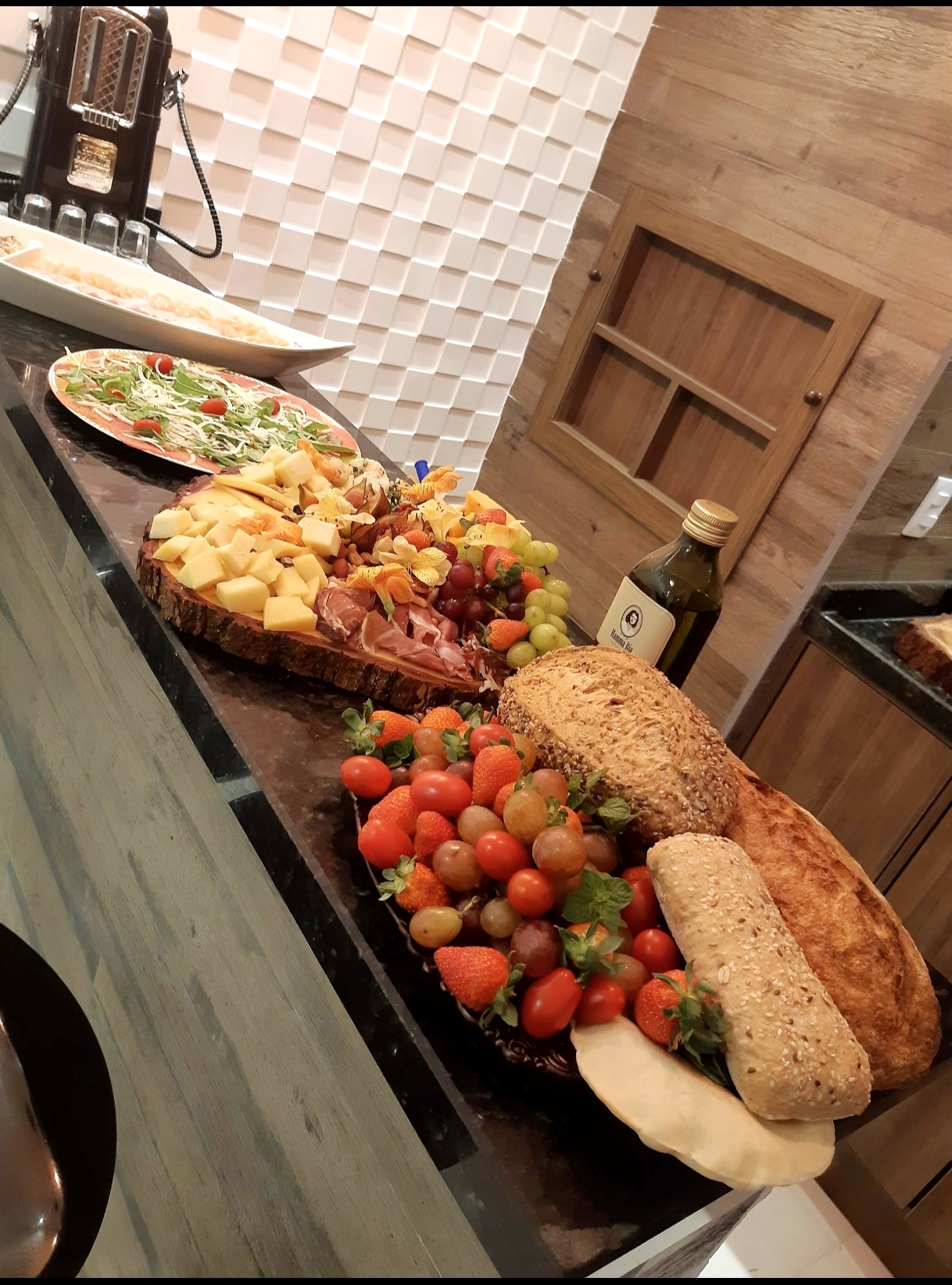 Tábua de frios, pães artesanais e frutas frescas dispostos sobre bancada de mármore